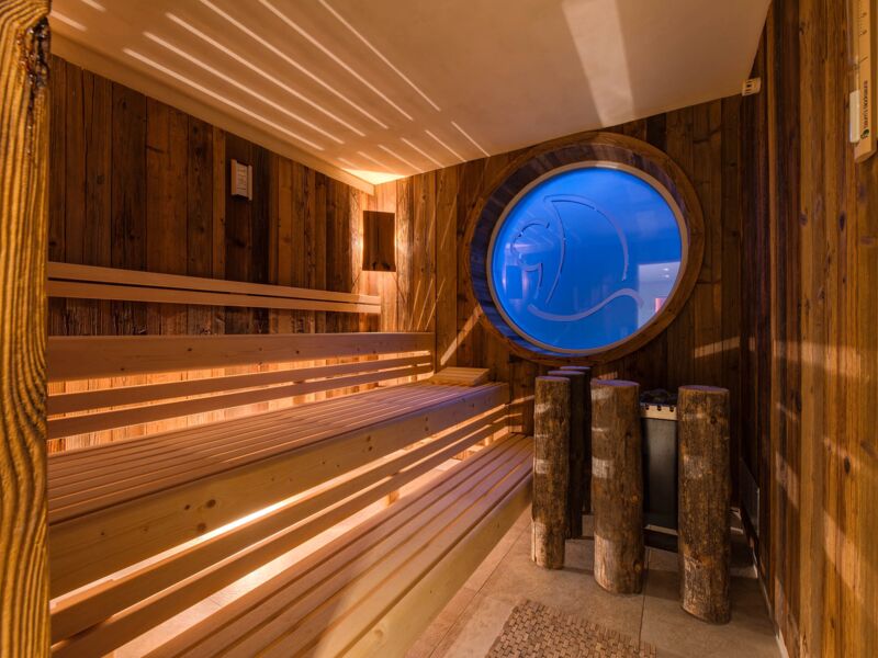 Das Bild zeigt die Saune im Wellness-Bereich vom Hotel ERholung. Man sieht viel Holz und im Hointergrund ein Ficht durchsichtiges Fenster mit dem Logo des Hotels.